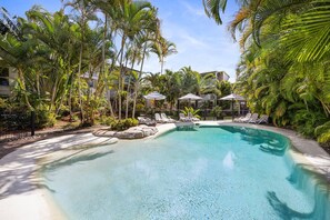 A pool surrounded by palm trees and lounge chairs, with a clear blue sky above. - Riverside Rest on Noosa River (Noosa)