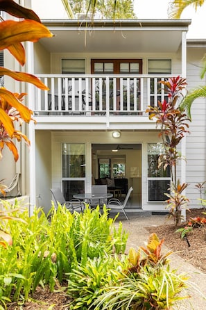 A two-story house with a balcony, a covered patio, and a variety of plants.