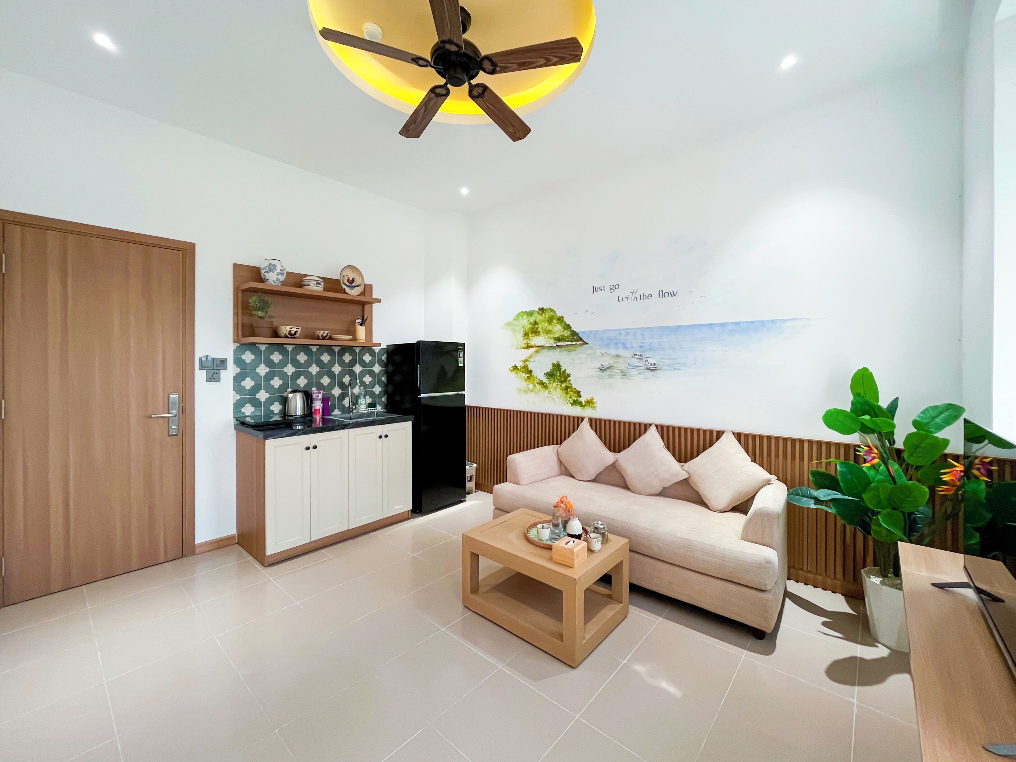 A modern living room with a sofa, coffee table, and a kitchen area with a refrigerator and cabinets.