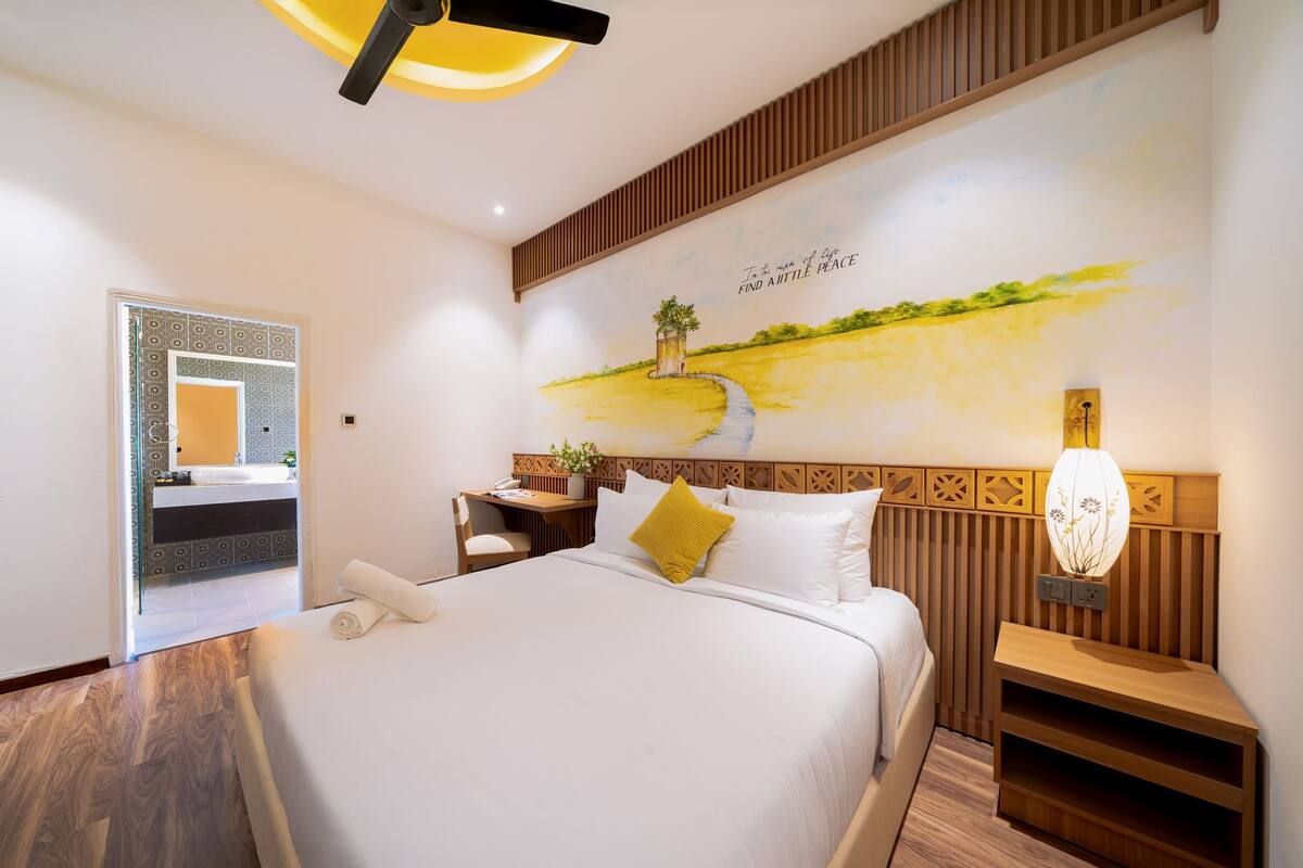 A hotel room with a bed, a nightstand, a desk, and a wall mural.
