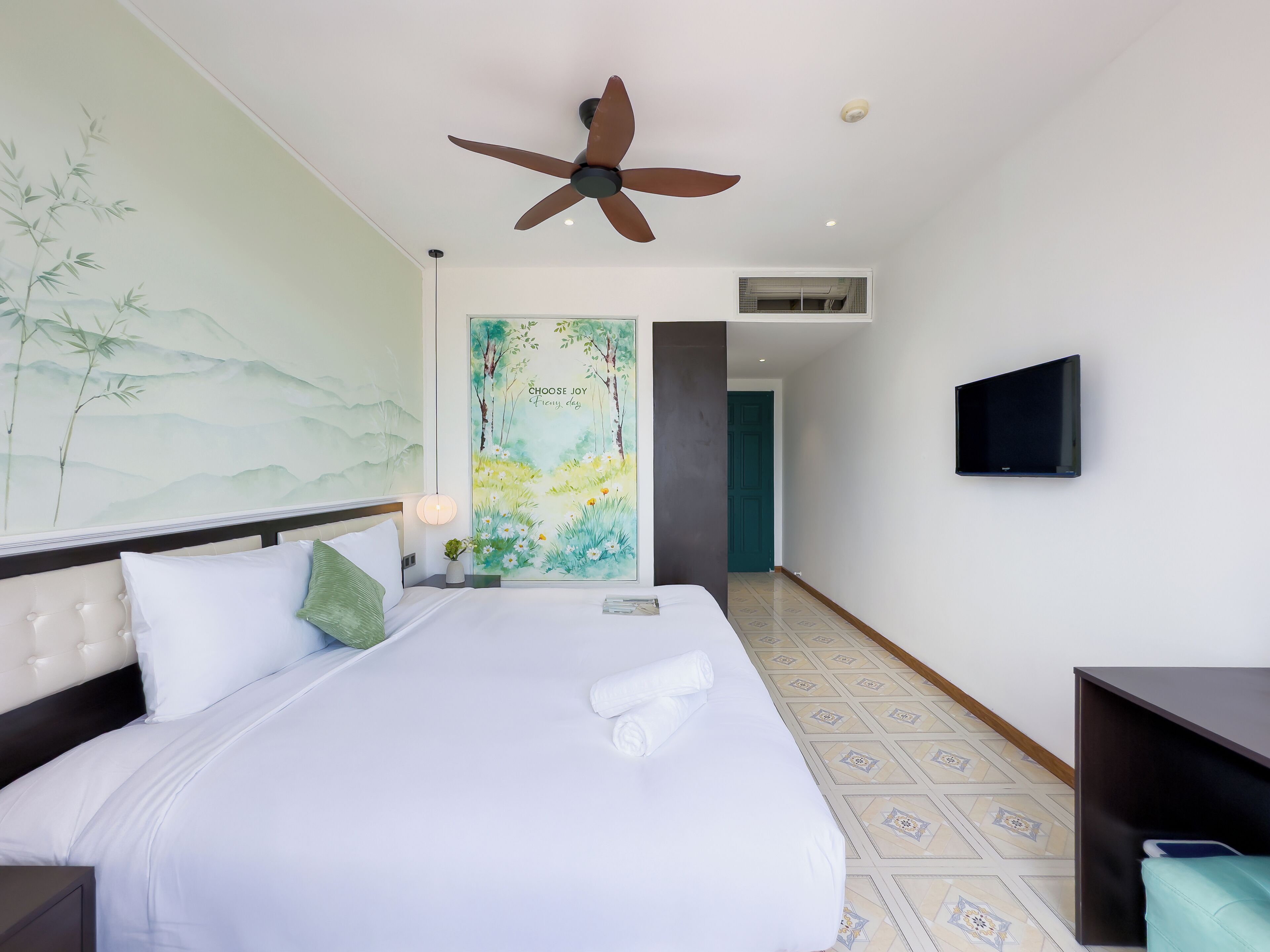 Une chambre d’hôtel avec un lit, un ventilateur de plafond, un téléviseur fixé au mur et un tableau.