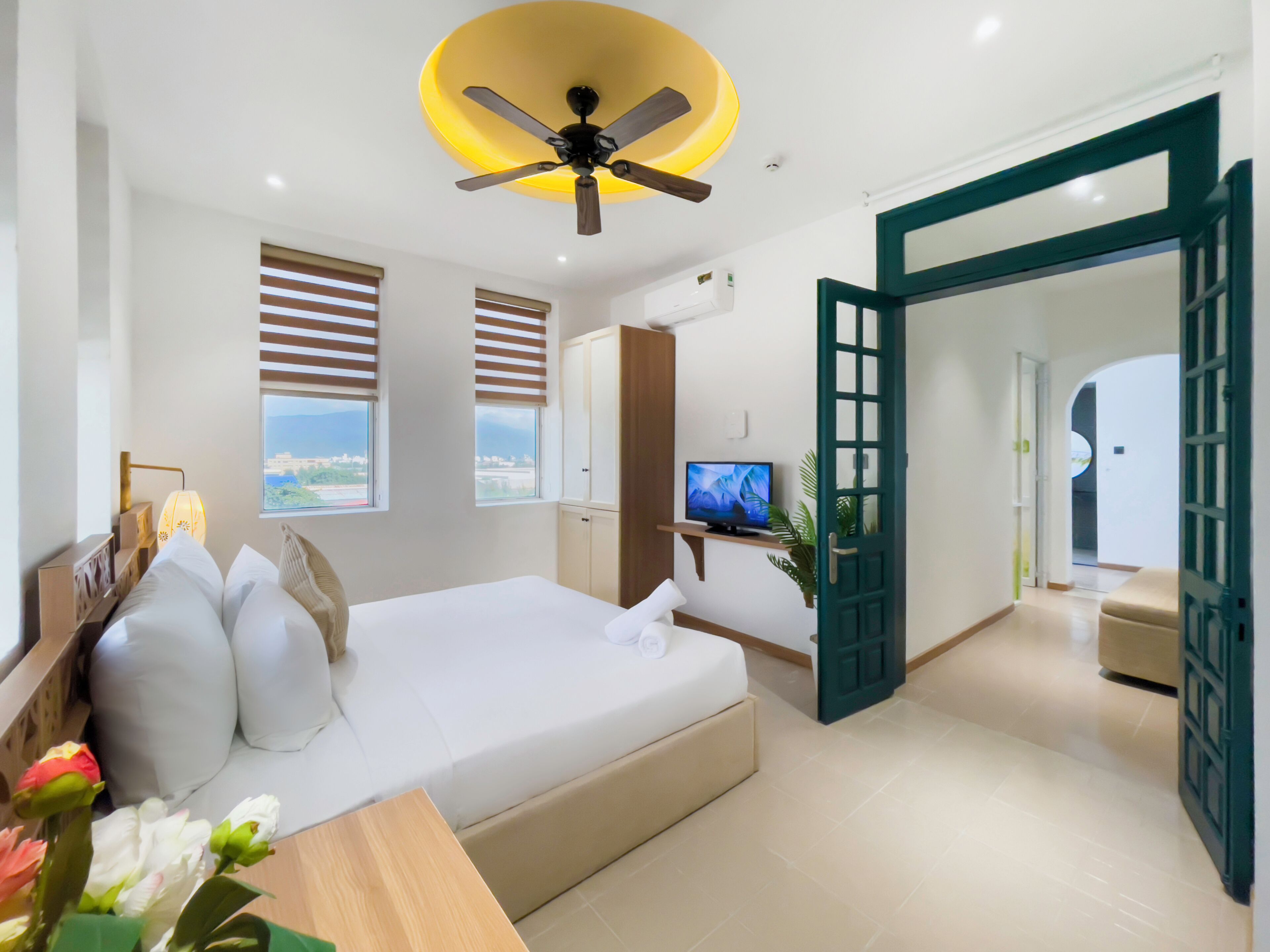 A modern hotel room with a bed, a TV, a ceiling fan, and a view of the sea.