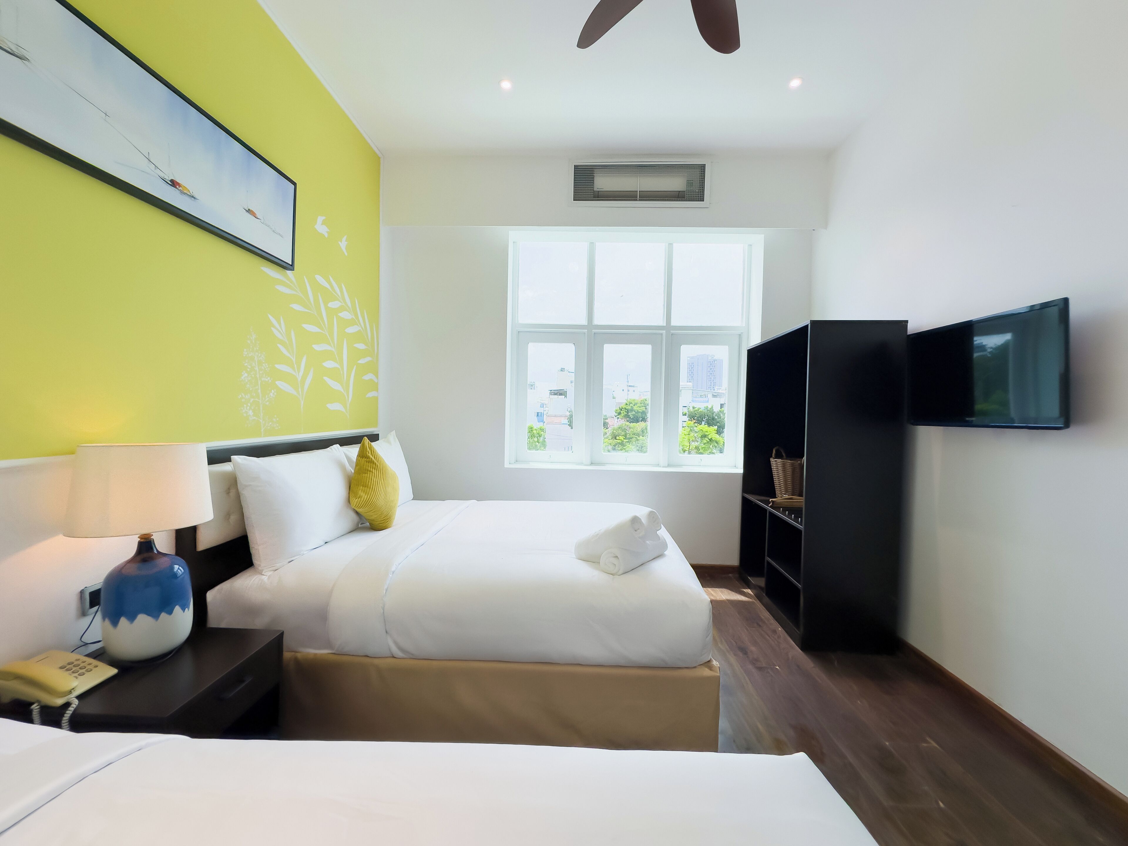 A hotel room with a bed, bedside table, lamp, and a TV mounted on the wall.