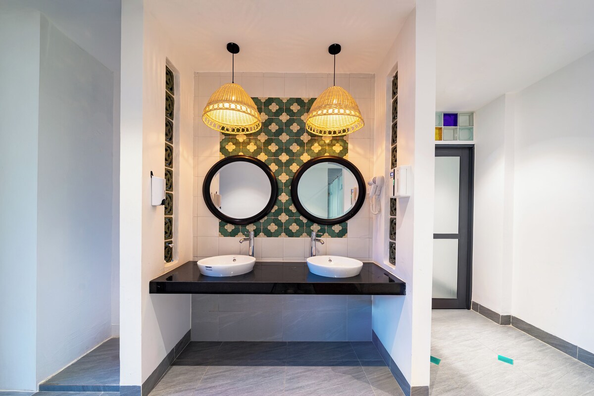 Un baño moderno con dos lavamanos, encimera negra, espejos decorativos y lámparas colgantes.