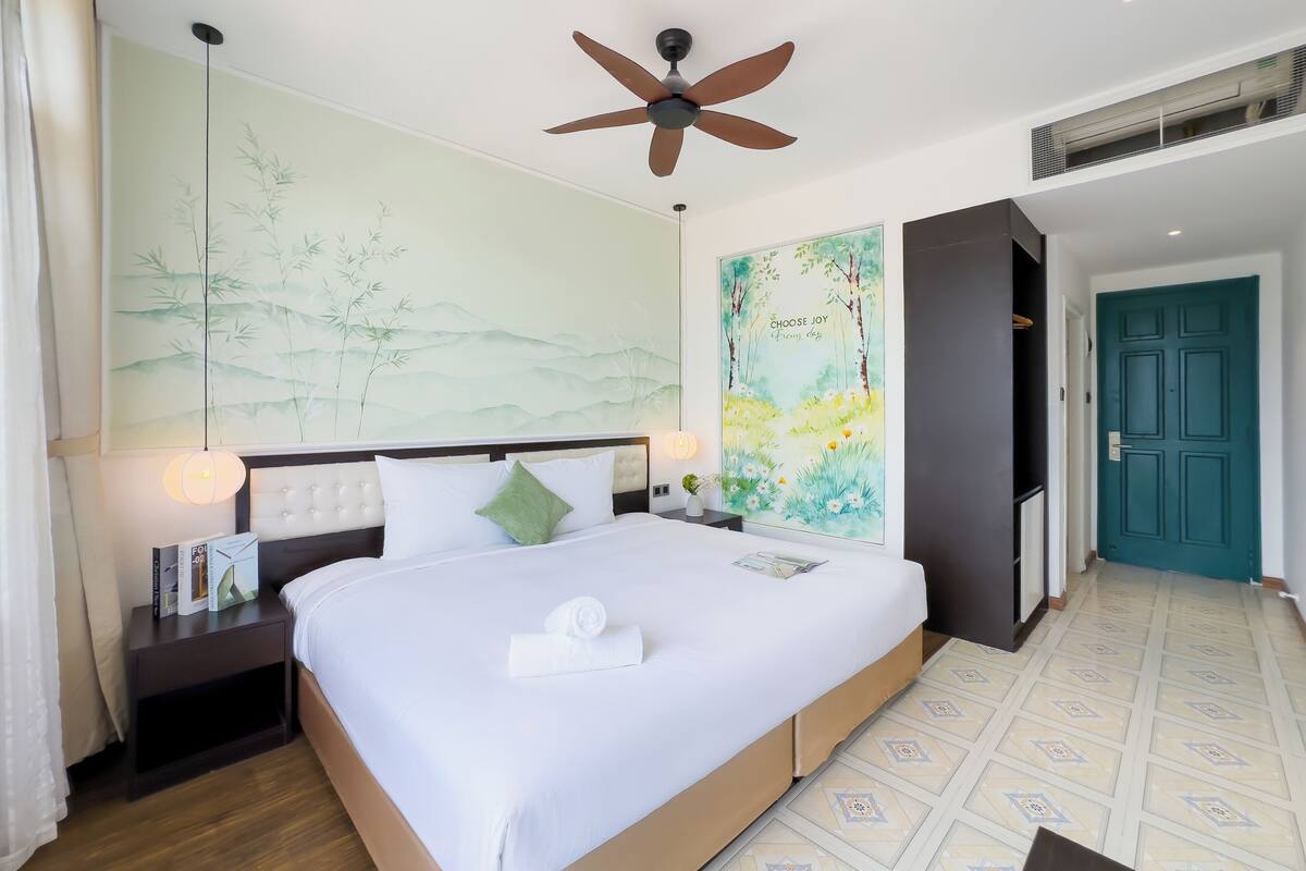 A hotel room with a large bed, a ceiling fan, a wall with a nature-themed mural, a door, and a patterned floor.