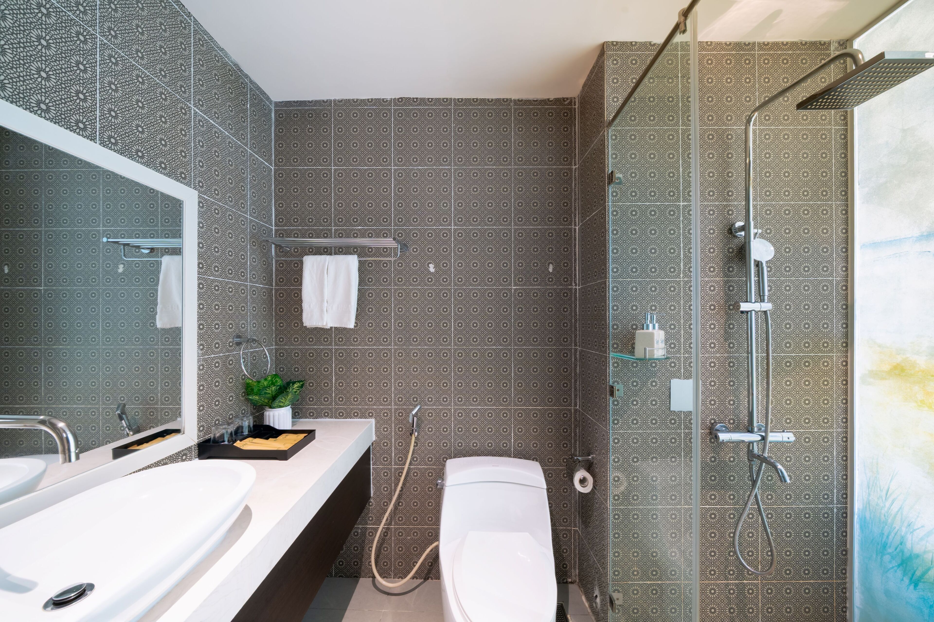 A modern bathroom with two sinks, a large mirror, a shower with a handheld showerhead, and patterned tiles.