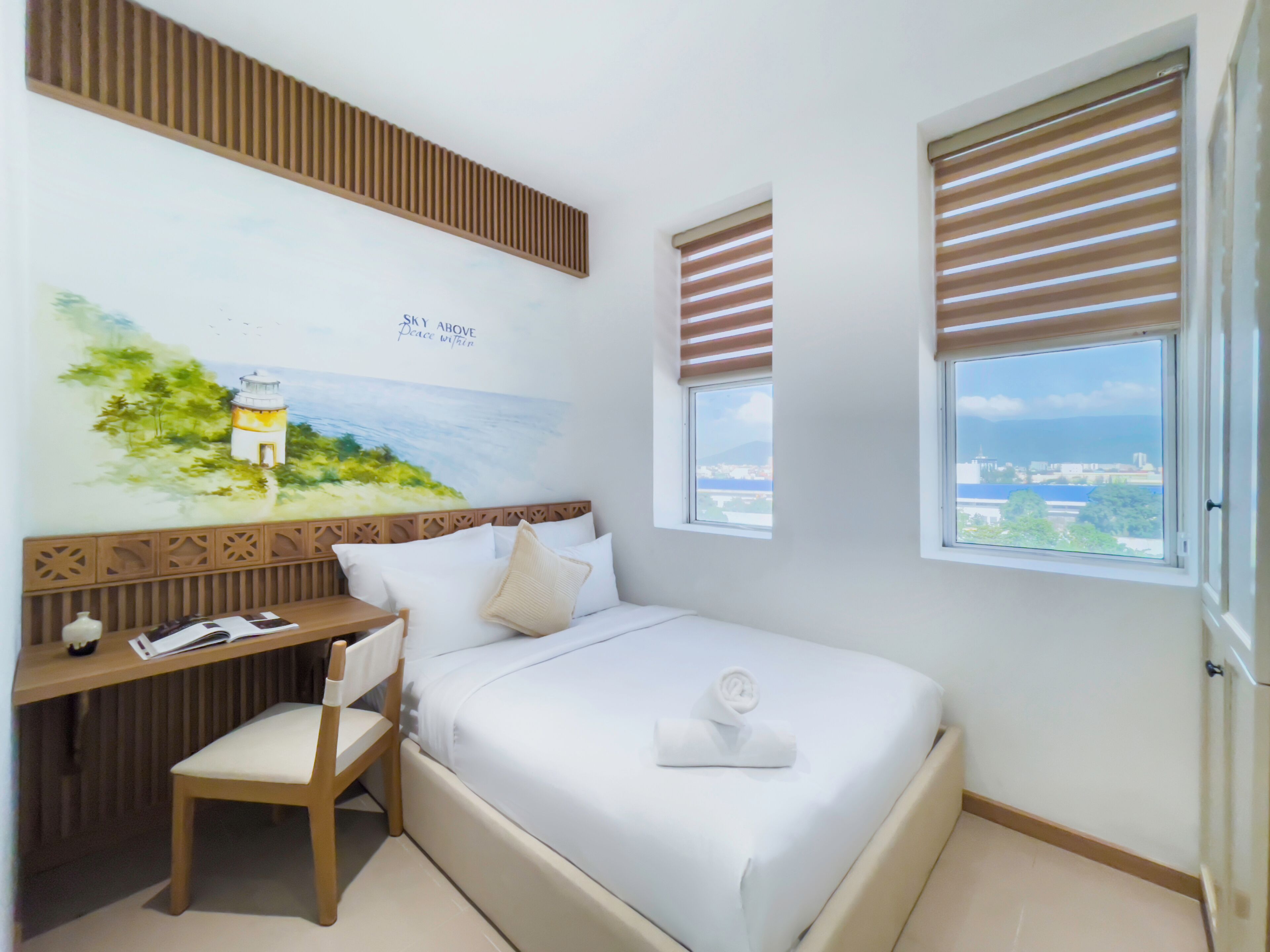 Ein Schlafzimmer mit Bett, Schreibtisch, Stuhl, einem Fenster mit Jalousien und einem Wandgemälde.