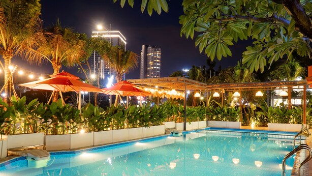 A swimming pool with surrounding palm trees and a covered area with umbrellas. - Sujet Beach Hotel &Apartment by Haviland (Da Nang)