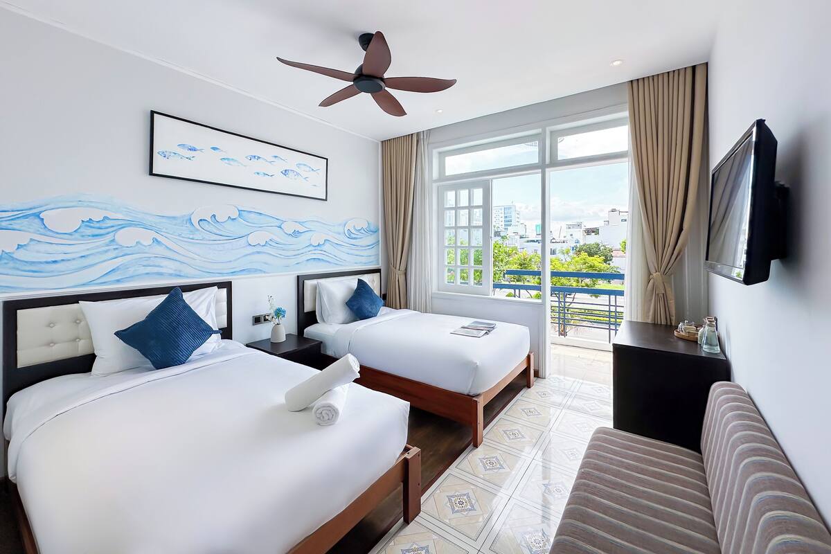 A hotel room with two beds, a ceiling fan, a large window with a view, and a mounted TV.
