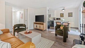 Een moderne woonkamer met een bank, salontafel en televisie. Er is een keuken met een eettafel en stoelen.