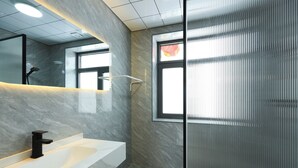 A modern bathroom with a white sink, a black faucet, and a glass shower enclosure.