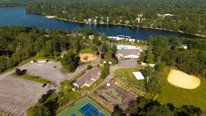 En vy från ovan av en fastighet vid en sjö, med en tennisbana, en parkeringsplats och en swimmingpool.