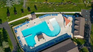 En bild tagen från luften som visar en pool med en ovanlig form, omgiven av blå solstolar och en möblerad sittgrupp under ett tak.