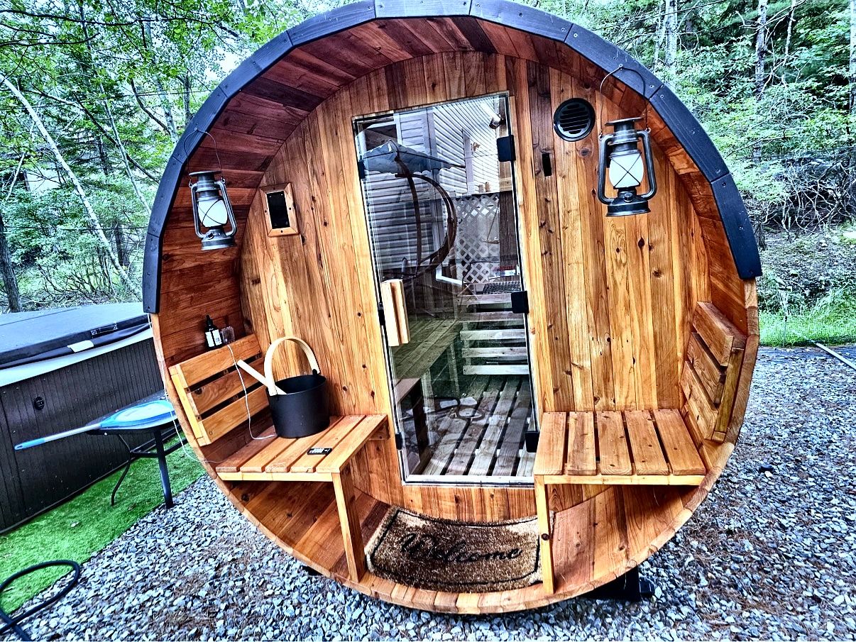 Una cabaña de madera con interior circular, un banco, una mesa, un farol y un ventanal pequeño.
