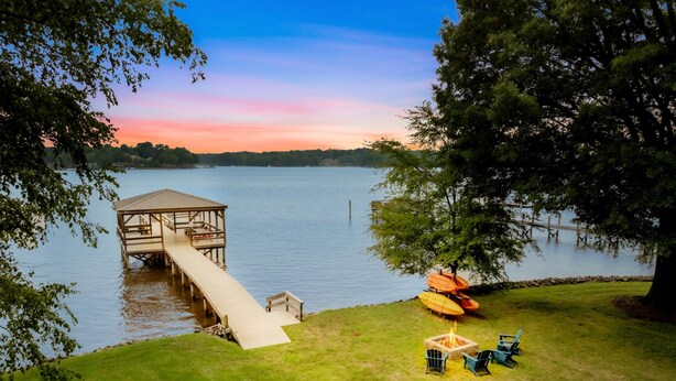 A wooden dock extending into a lake with a grassy area and a fire pit. - Huge Covered Dock, Firepit, Kayaks, Foosball (Mooresville)
