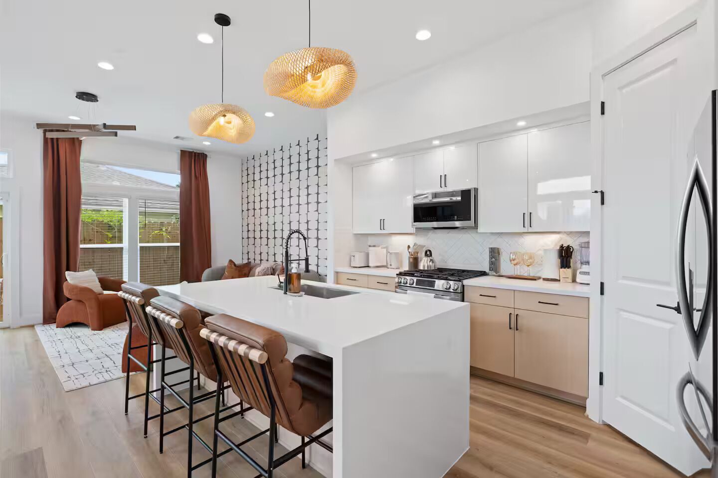 A modern kitchen with a central island, bar stools, a microwave, stove, and pendant lighting.