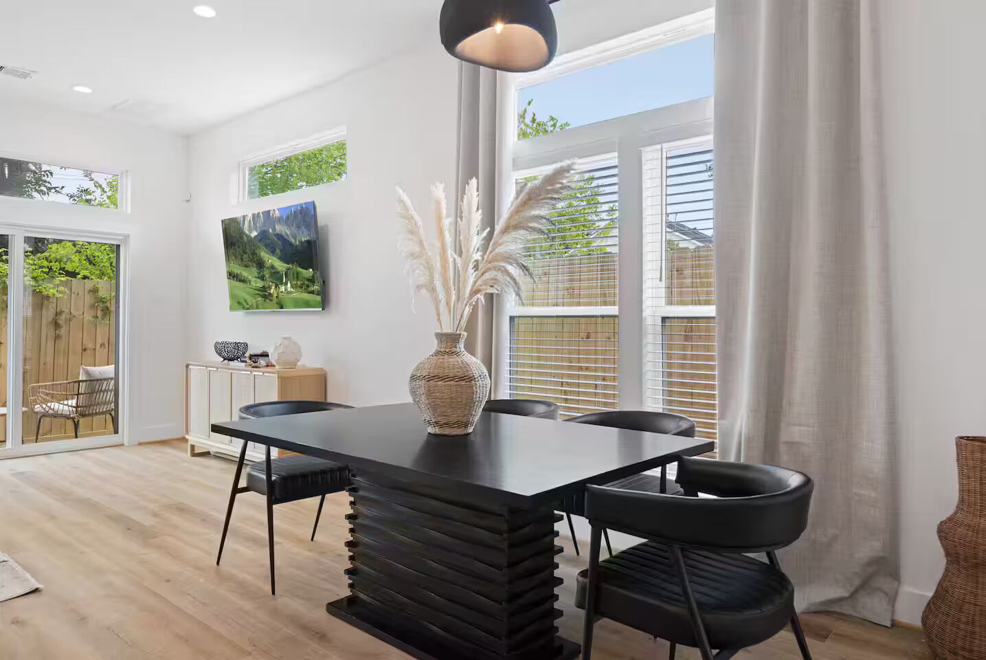 A modern dining area with a black table, white walls, and large windows.