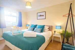 A neatly arranged bedroom with a bed, bedside tables, a hanging chair, and a window with curtains. - Merriotts Court by Tŷ SA (Newport)