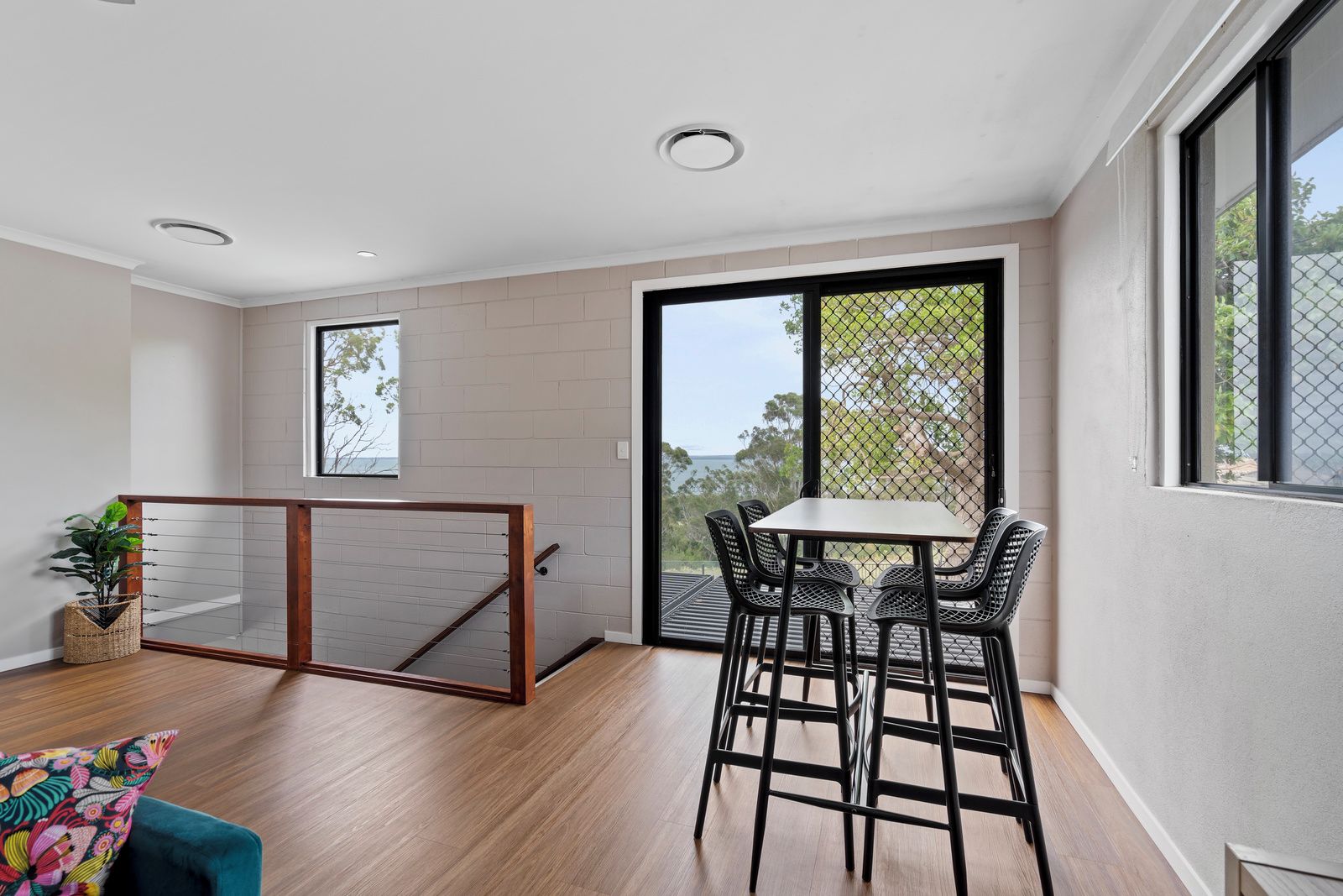 Un interior moderno con suelo de madera, un balcón con mesa y sillas, y vistas al exterior.