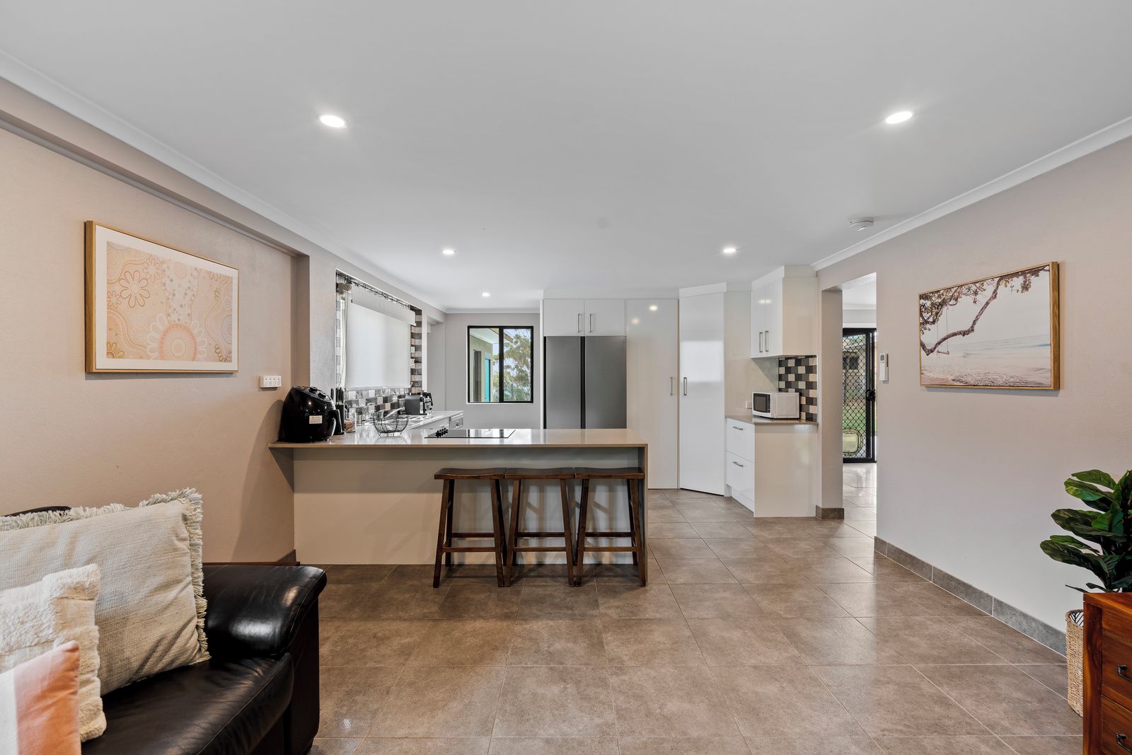 A modern kitchen with a central island, a dining area with a black leather couch, and a view of the outdoors.