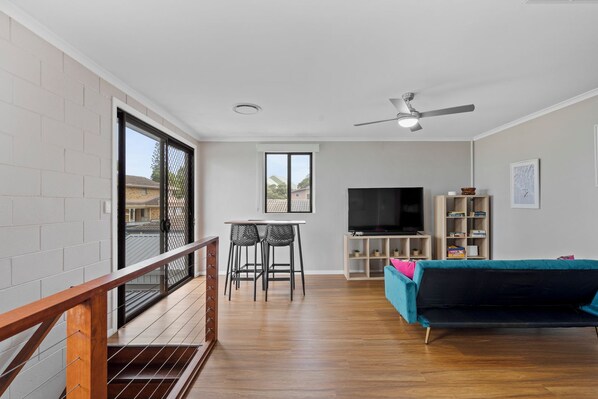 A modern living room with a TV, seating, and a balcony with a railing.