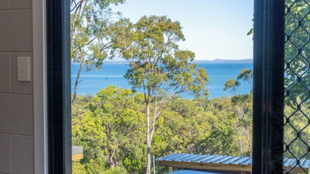 A view from a window overlooking a coastal landscape with trees and a clear sky.