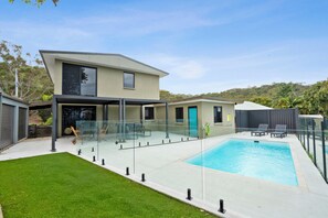 A modern house with a swimming pool, a covered patio, and a well-maintained lawn.