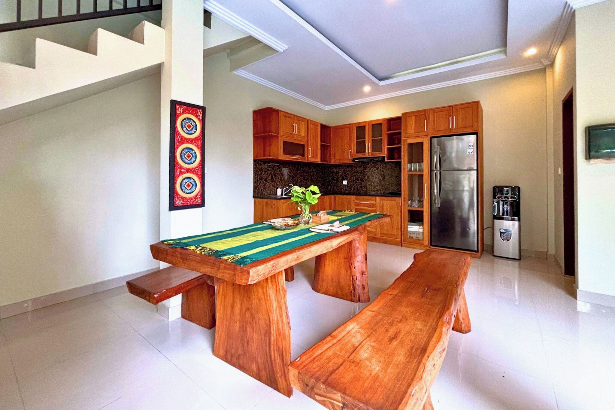A modern kitchen with wooden cabinets, a stainless steel refrigerator, and a dining table with benches.