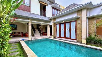 Una casa de dos pisos con piscina, un patio cubierto y una escalera que conduce al piso superior.