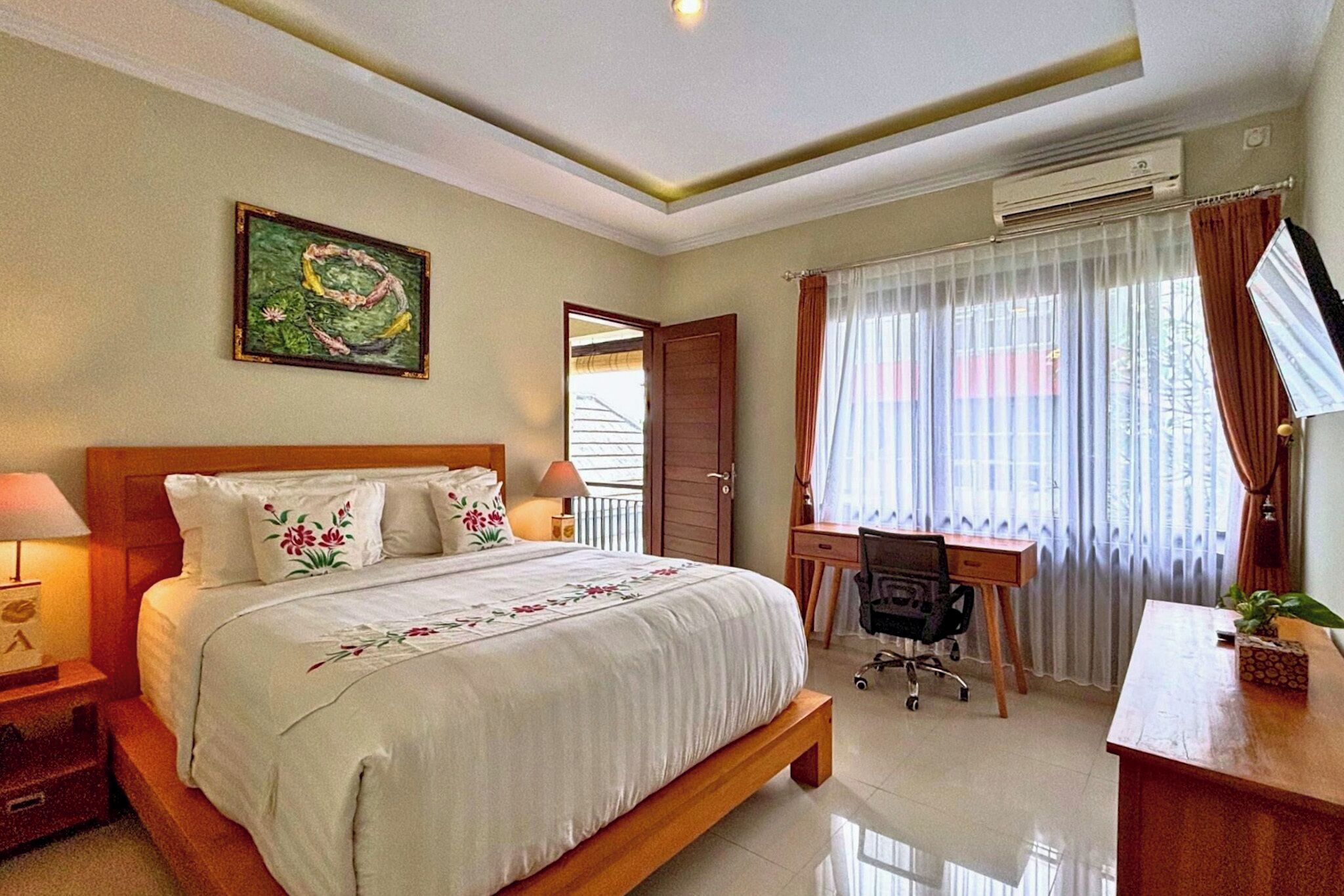 A hotel room with a large bed, a desk, and a chair. There is a window with curtains, an air conditioning unit, and a painting on the wall.