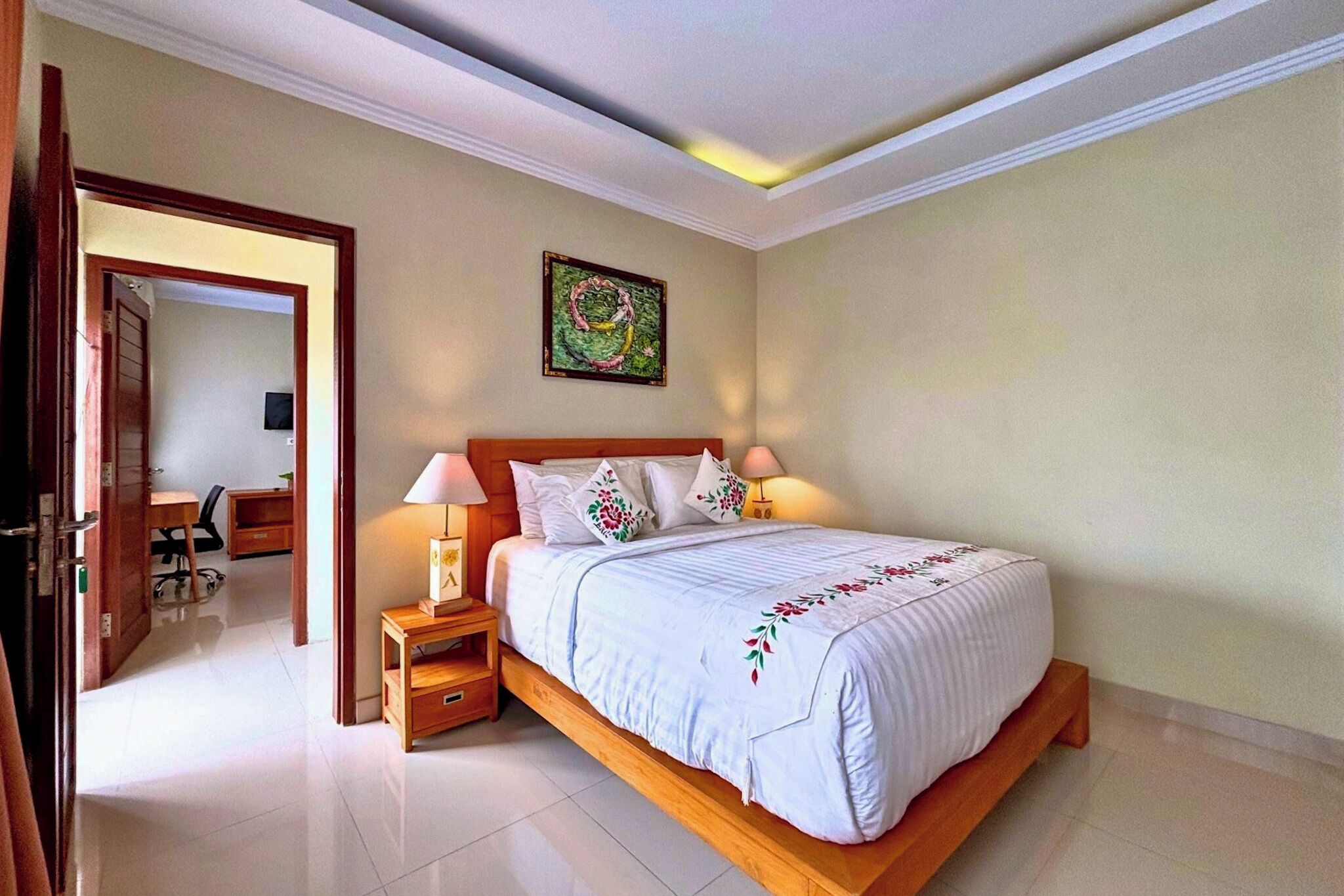 A bedroom with a large bed, bedside lamps, a wooden nightstand, a desk, and a chair.