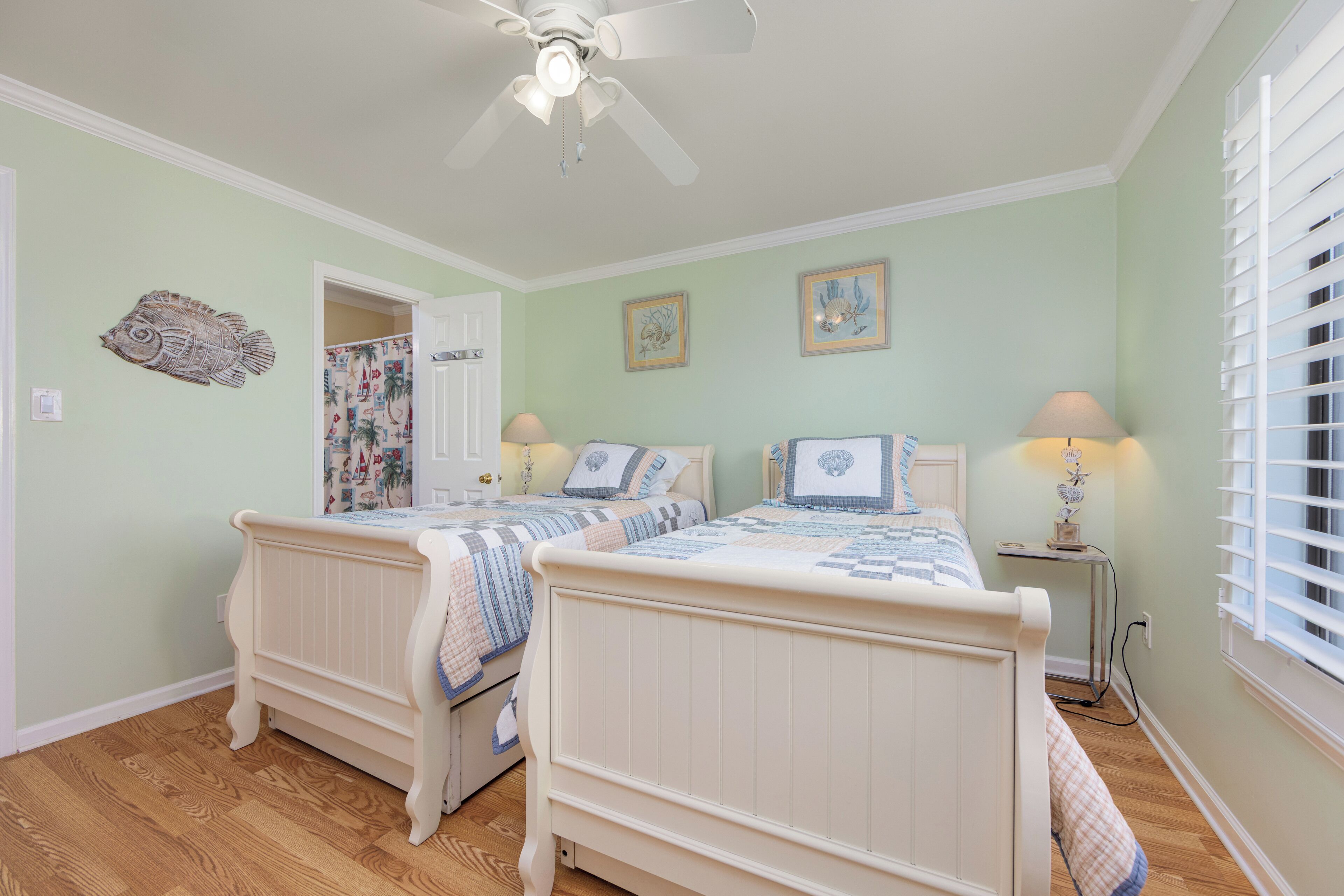 A bedroom with two beds, a ceiling fan, and a window with blinds.