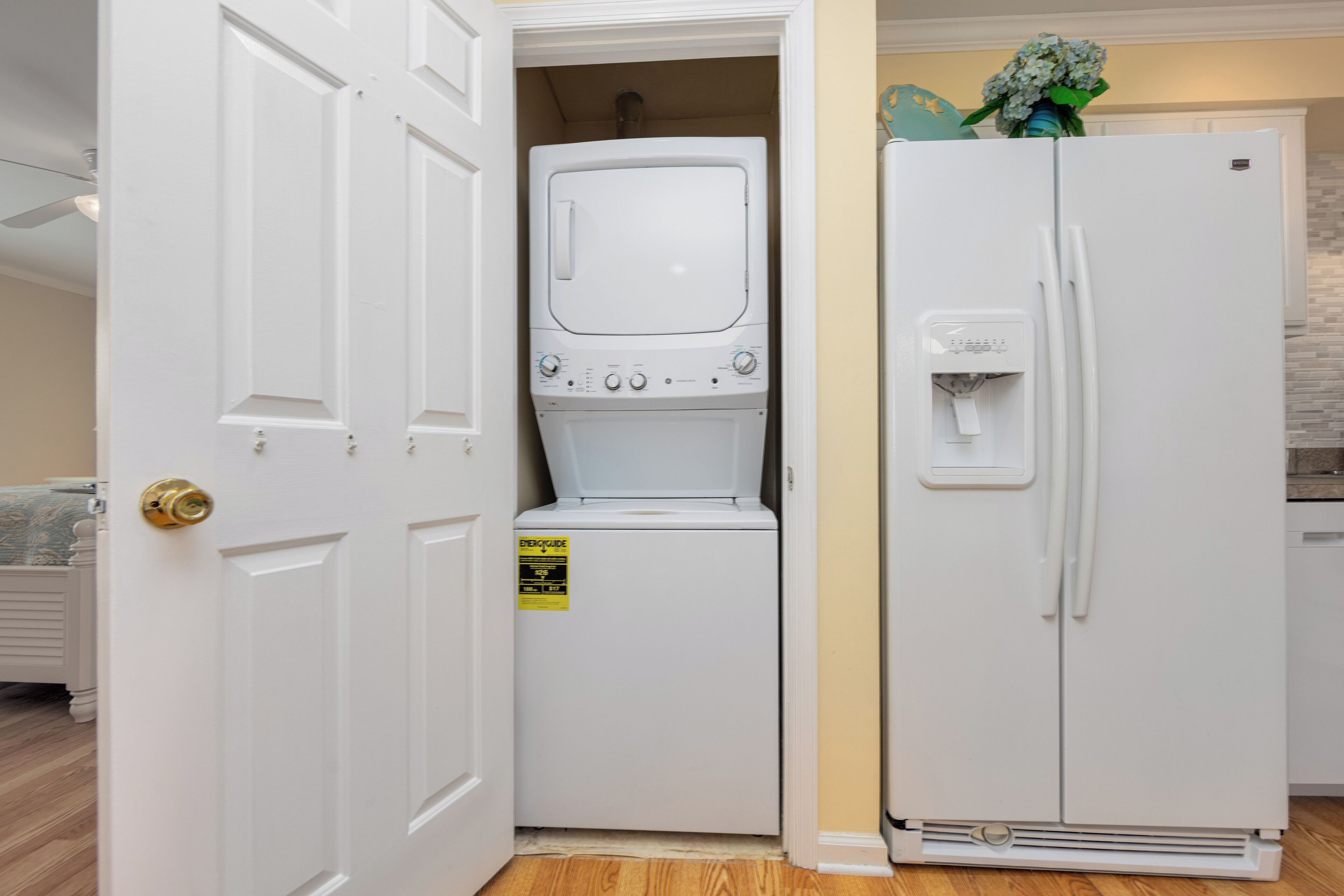 Una cocina compacta con un refrigerador blanco, una lavadora y una puerta que da a otra habitación.