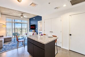 A modern kitchen with a granite countertop, a dining area with a glass table, and a large window with blinds. - Explore Downtown Phoenix, AZ | Pool, Gym & Parking (Phoenix)