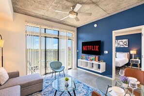 A modern living room with a ceiling fan, a TV mounted on the wall, a sofa, a coffee table, and a dining area with a table and chairs.