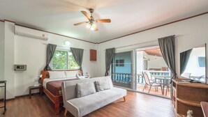 Een slaapkamer met een bed, een bank, een plafondventilator, een raam met gordijnen, een balkon met een tafel en stoelen, en een televisie op een dressoir.