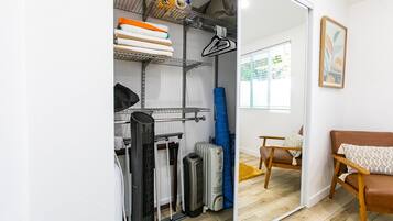 Ein kleines Zimmer mit einem Bett, einem Sessel und einem Schrank mit Regalen und einem Heizkörper.