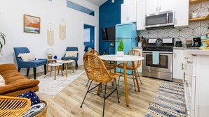 Une cuisine moderne avec des meubles blancs, un four à micro-ondes et une cuisinière. On y trouve également un coin repas avec des chaises en osier et une table ronde.