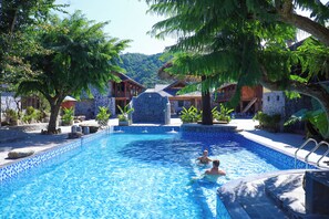 A swimming pool surrounded by tropical trees and wooden buildings. - HaGiang Go Ecolodge (Ha Giang 1)
