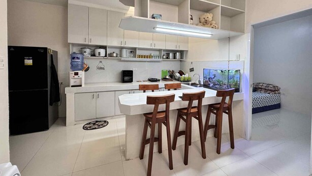 Eine moderne Küche mit weißen Schränken, einem schwarzen Kühlschrank, einem Esstisch mit Holzstühlen und einem Aquarium auf der rechten Seite.