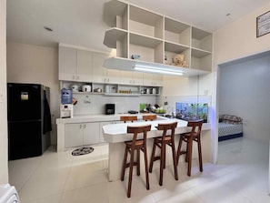 A modern kitchen with white cabinets, a black refrigerator, a dining table with wooden chairs, and a fish tank on the right.
