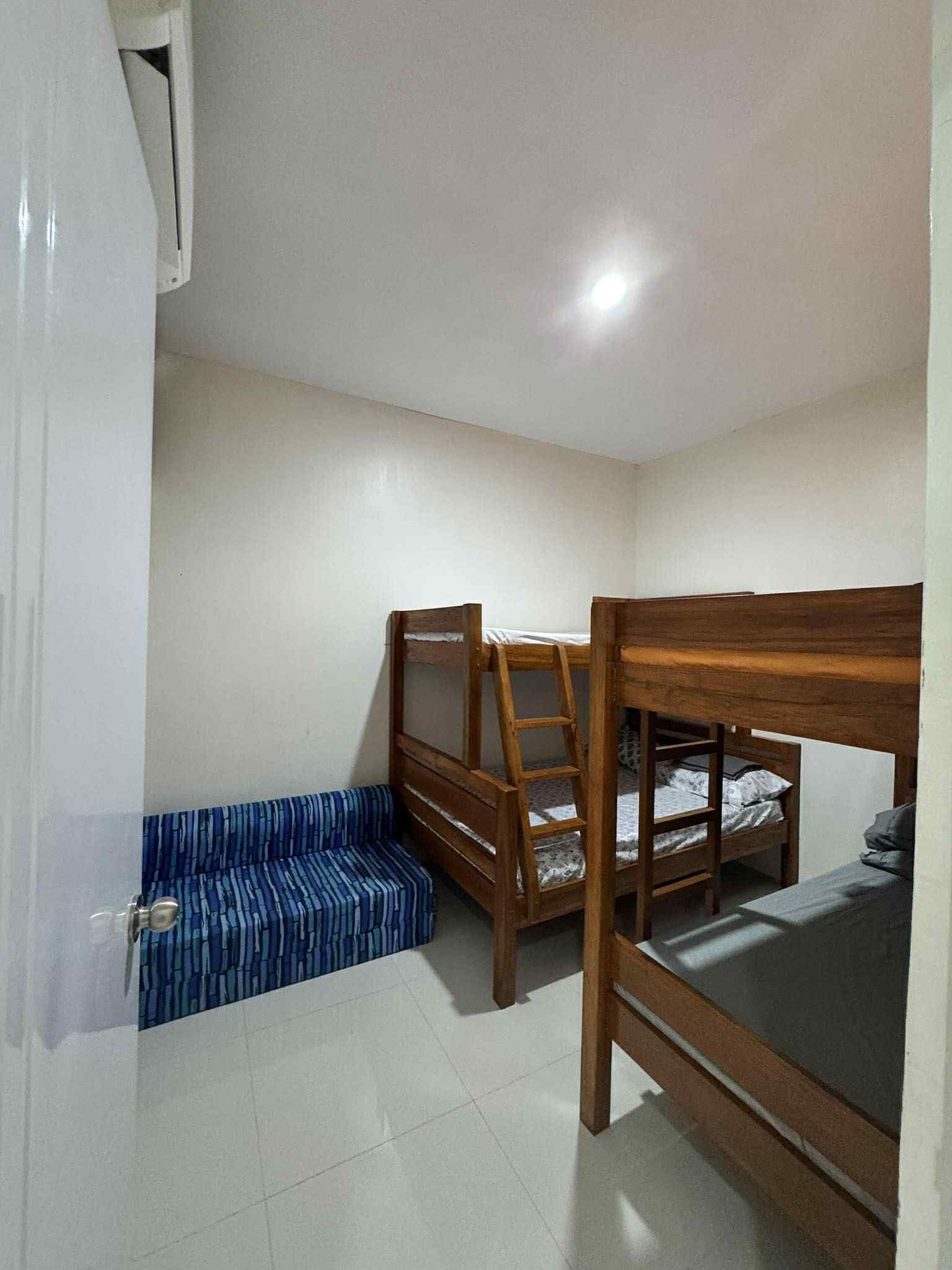 Una habitación con literas, un banco azul a rayas y un equipo de aire acondicionado blanco.