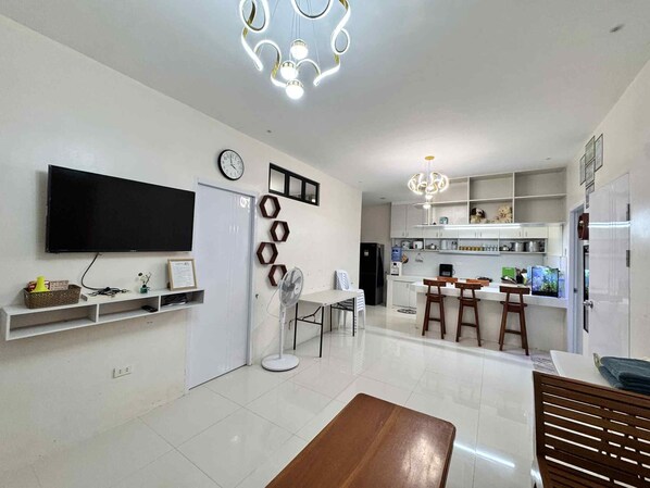 A modern kitchen with white cabinets, a built-in oven, and a refrigerator. There is a dining area with a wooden table and chairs.