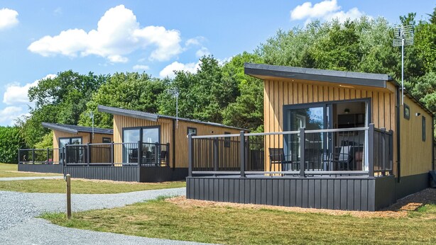 A row of modern cabins with large windows and a deck, surrounded by trees and a clear sky.