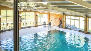 An indoor swimming pool with clear water, surrounded by windows and a brick wall.