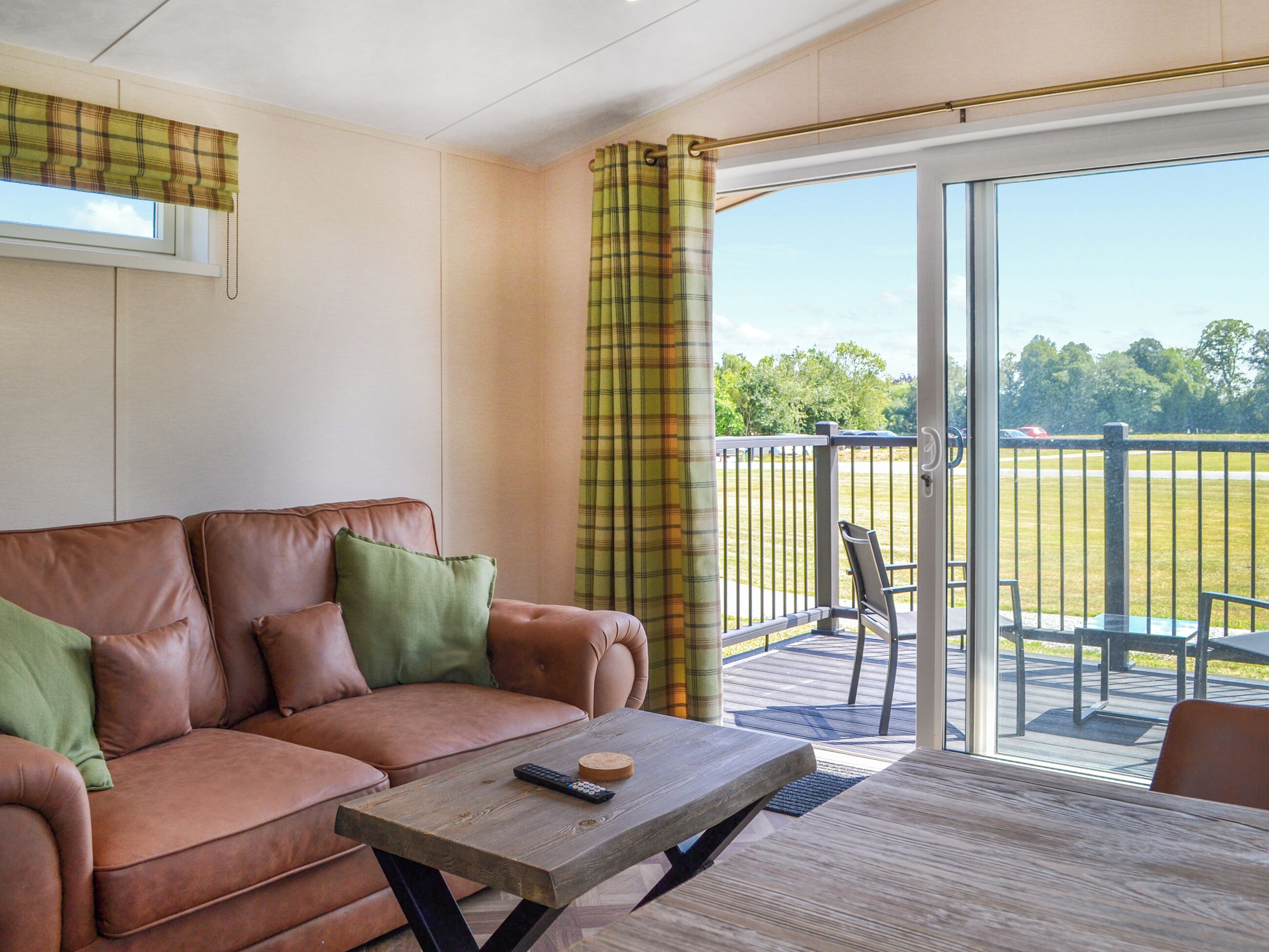 A cozy living room with a brown leather sofa, a wooden coffee table, and a view of a grassy field through a sliding glass door.