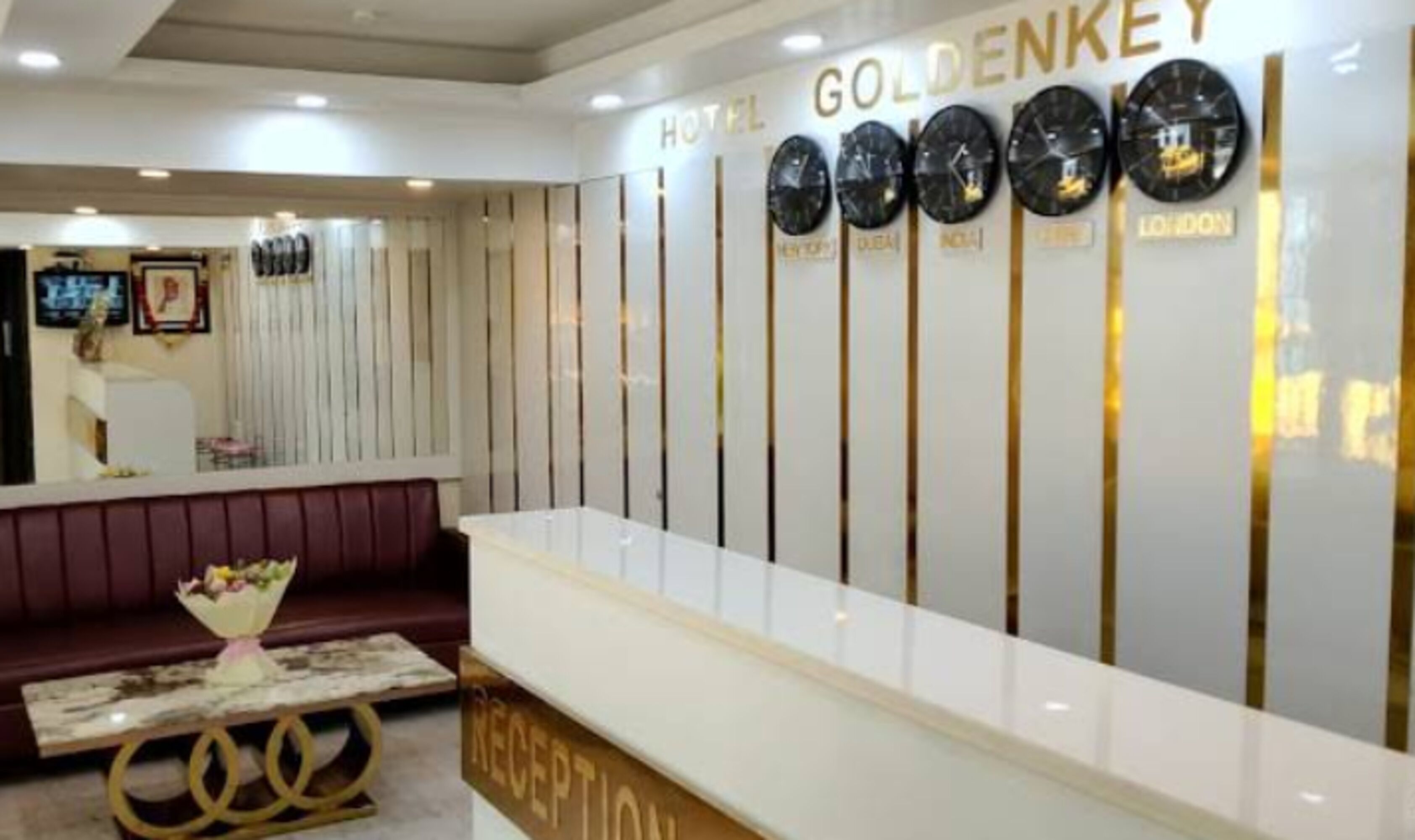 A hotel reception area with a reception desk, a sofa, and a wall with clocks indicating different time zones.