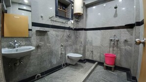A bathroom with a sink, toilet, shower, and a red bucket. - Hotel Goldenkey (Kolkata)