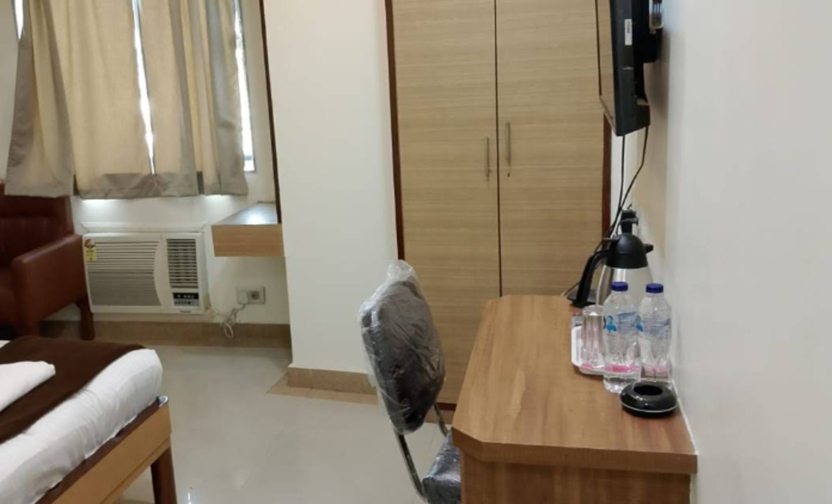 A hotel room with a bed, a desk with a lamp, a chair, and a wardrobe.