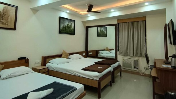 A hotel room with three beds, a desk, a chair, and a ceiling fan. - Hotel Goldenkey (Kolkata)